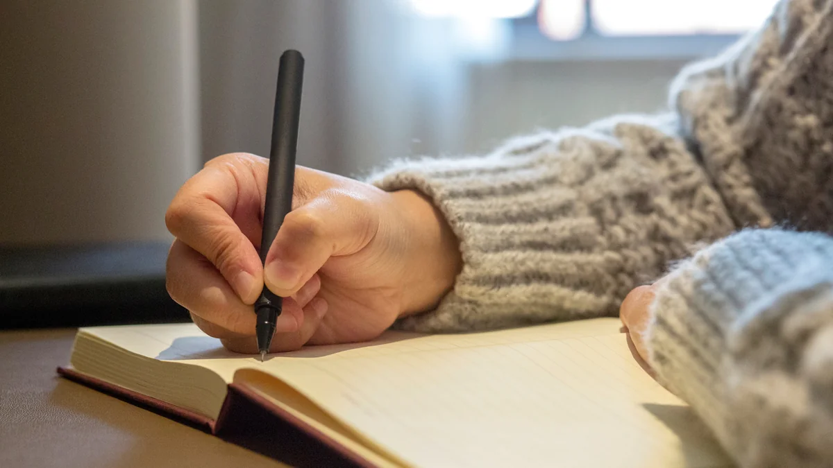 A hand in a wool sweater writing in an open notebook