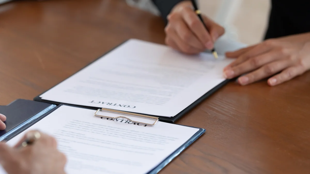 Two people signing a printed contract at a wooden table