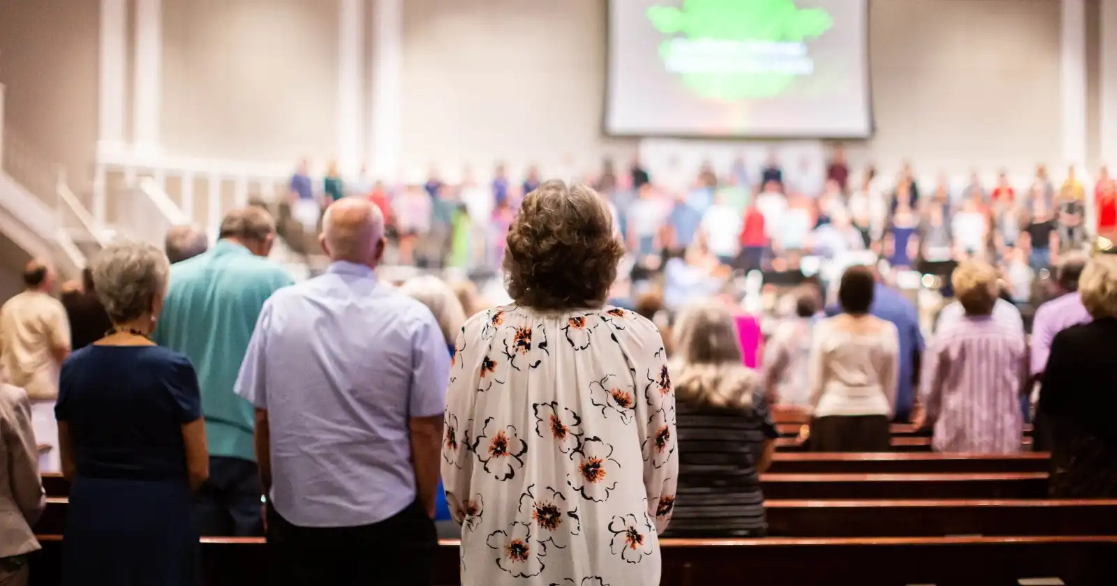 Congregation standing in church pews facing the stage during a Sunday morning worship service